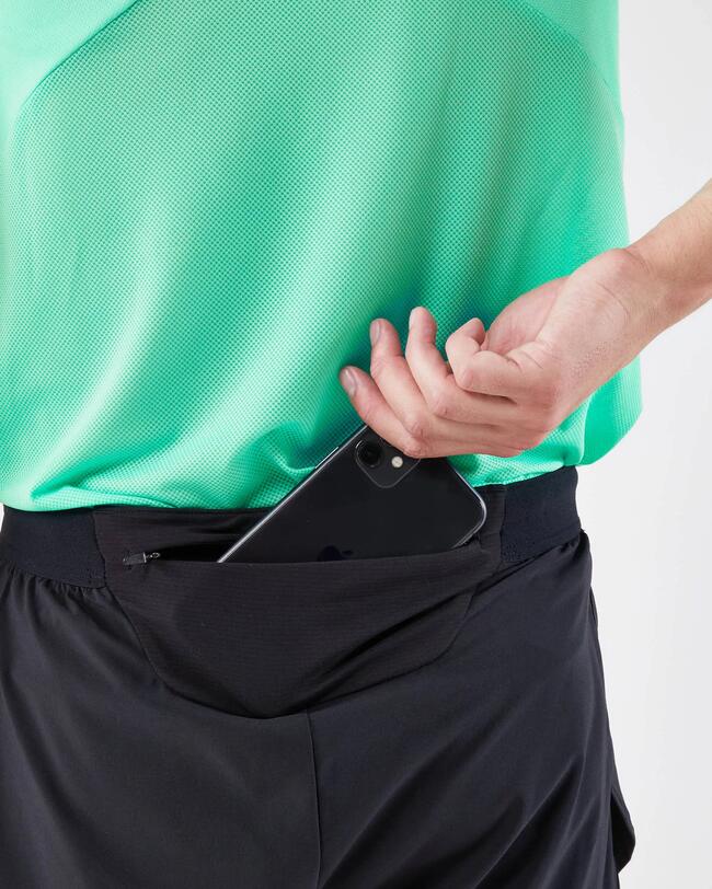 Grünes Shirt, schwarze Hose, Hand steckt Smartphone in Hintertasche, sportliche Textur.