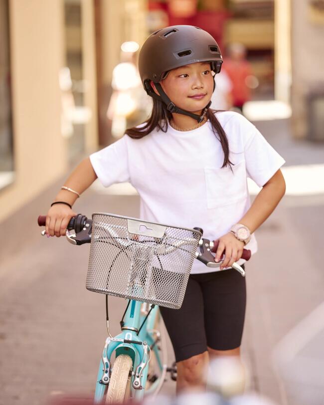 Kind mit schwarzem Helm schiebt türkises Fahrrad durch eine Straße