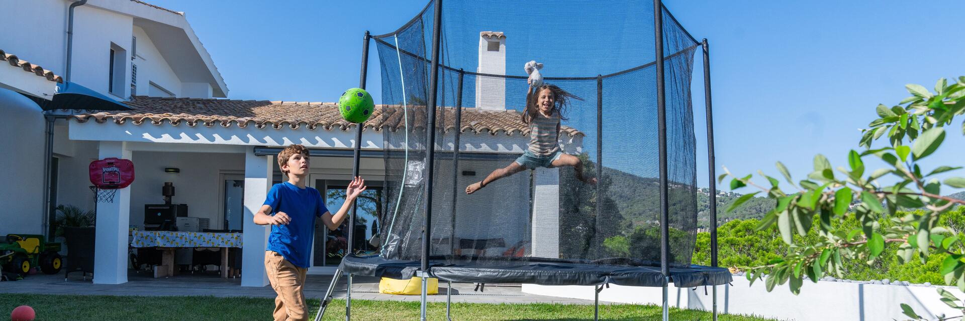 Dziewczynka skacząca na trampolinie ogrodowej dla dzieci przed domem