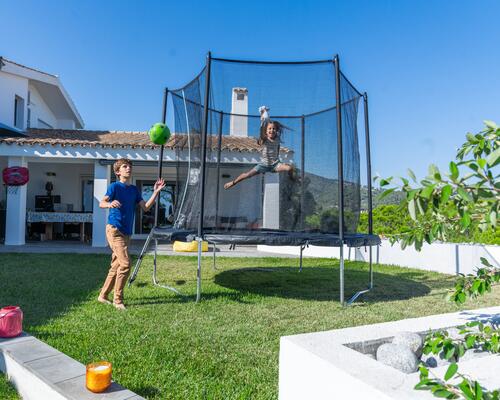 Dziewczynka skacząca na trampolinie ogrodowej przed domem 