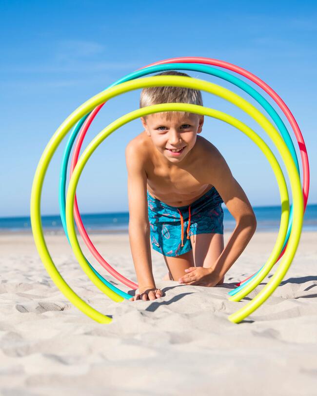 Ein Junge krabbelt durch Gymnastikreifen am Strand.