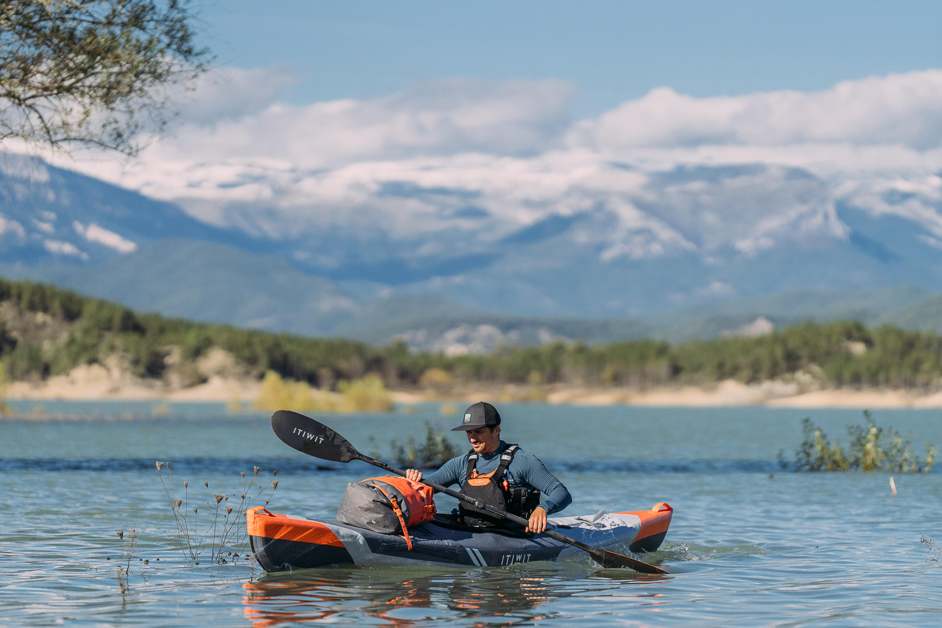 Angler paddling a fishing kayak across a mountain lake