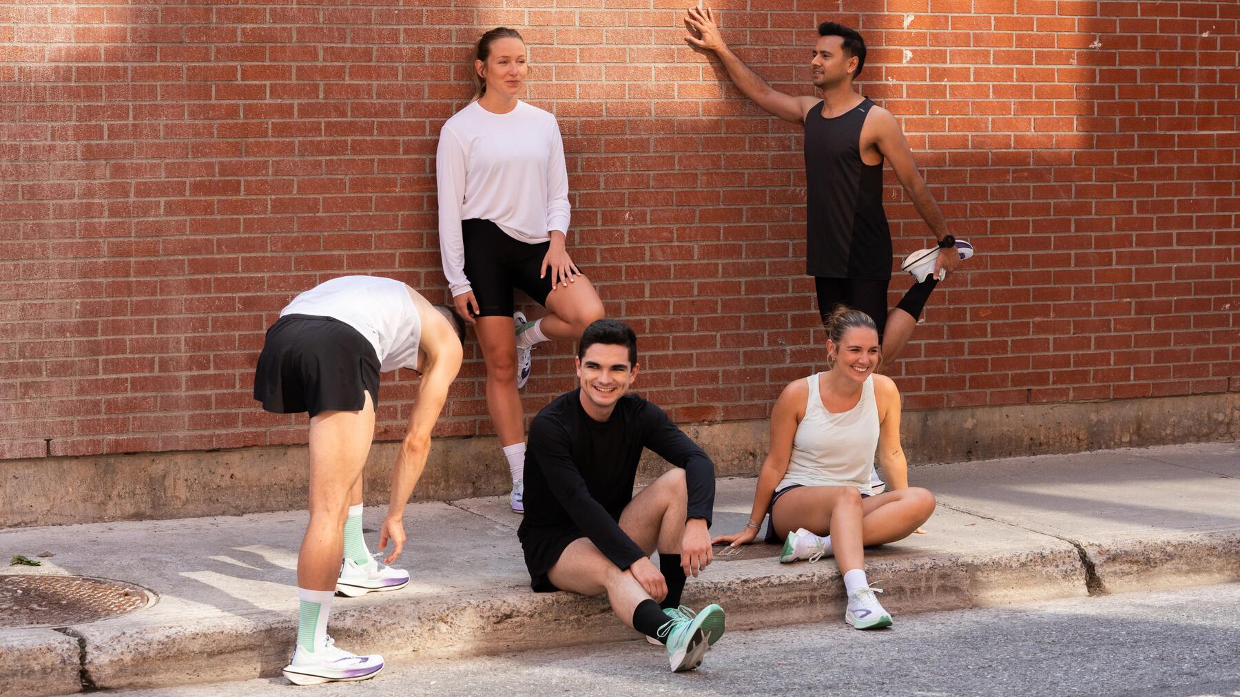 Fünf junge Menschen in Sportkleidung vor roter Backsteinwand, entspannte Atmosphäre, helle Farben, glatte und feste Texturen.
