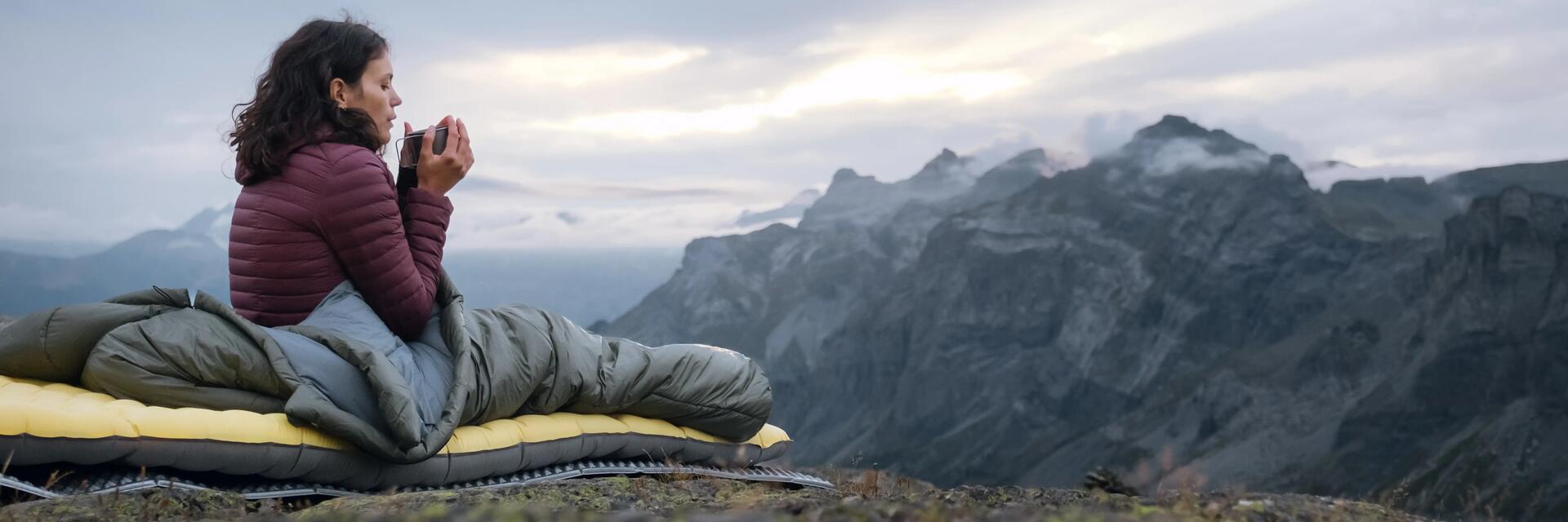 A woman lays on an inflatable sleeping mattress in front of the mountains