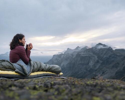 A woman lays on an inflatable sleeping mattress in front of the mountains