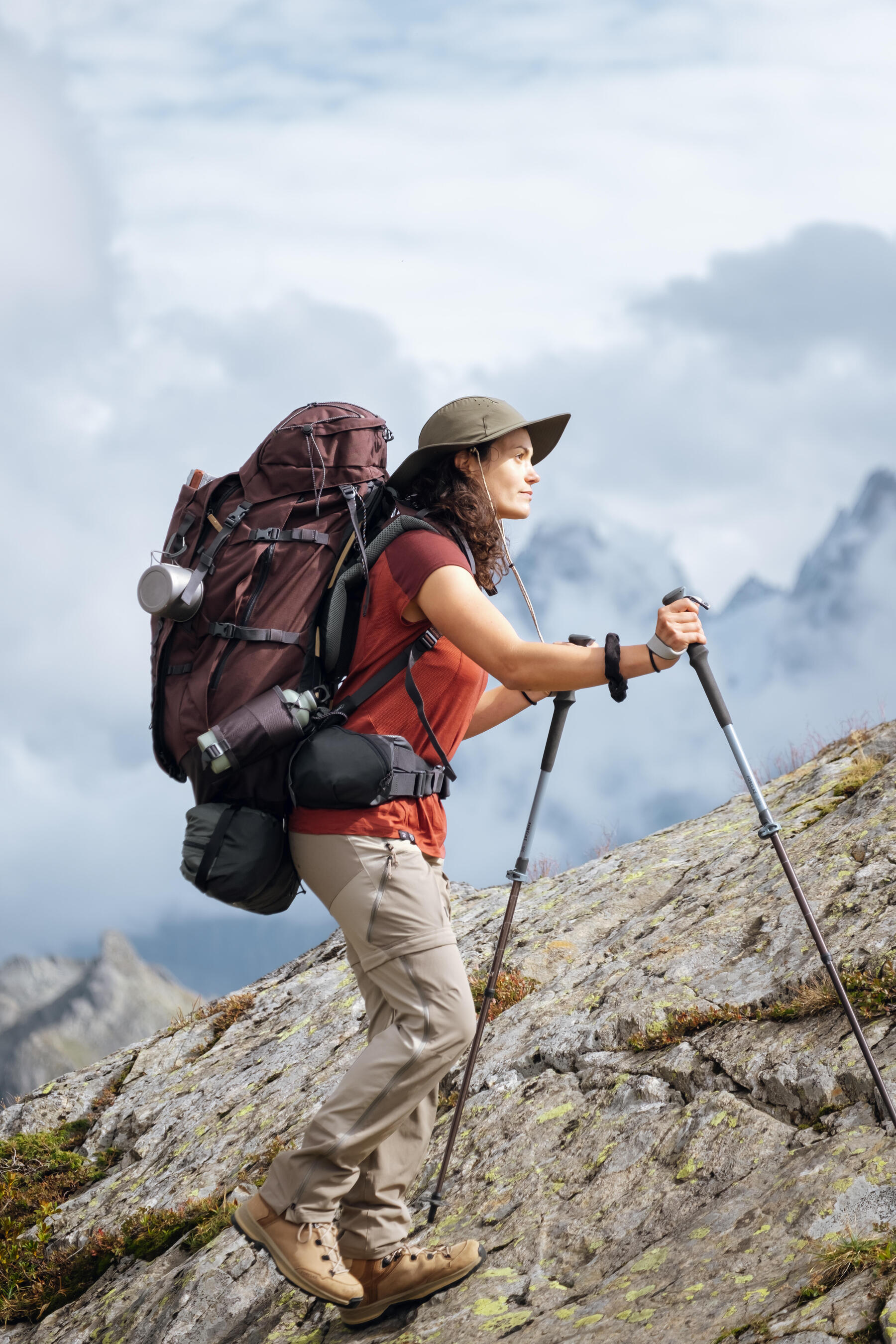 Kobieta wędrująca po górach do schroniska niosąc na plecach plecak turystyczny z przyczepionym kubkiem turystycznym 