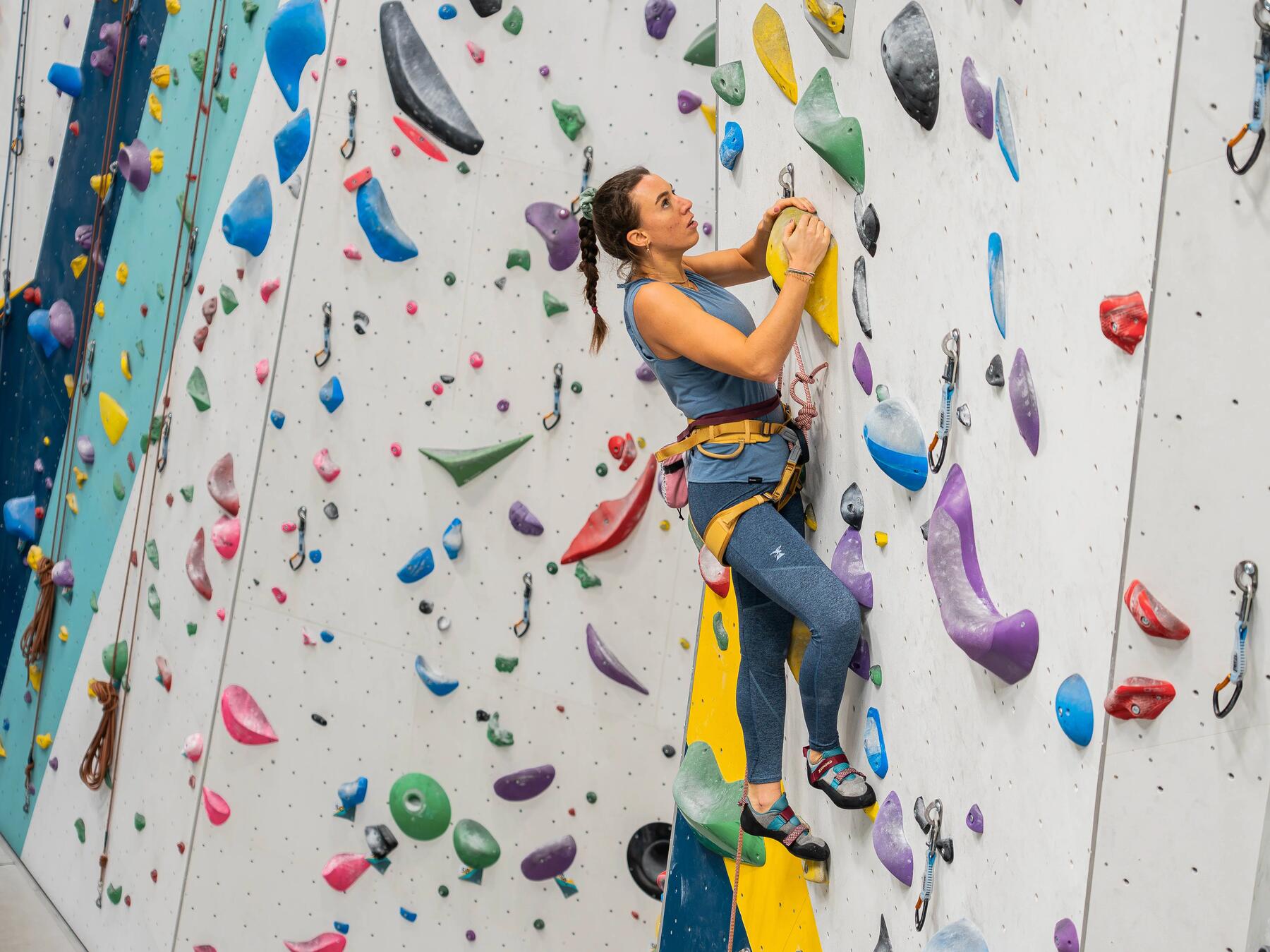 Kobieta w uprzęży i butach wspinaczkowych trenująca wspinaczkę sportową na ściance wspinaczkowej