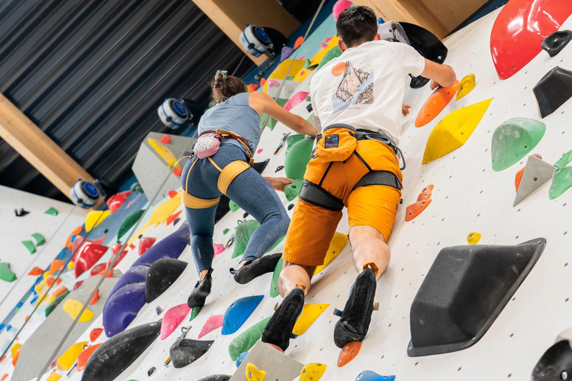 Man and woman doing indoor wall climbing wearing climbing harnesses?