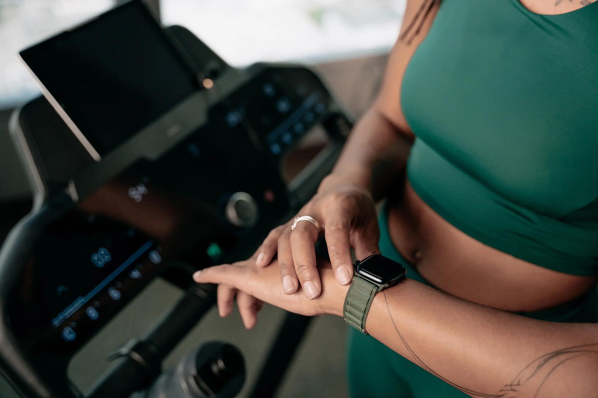 Kobieta stojąca na bieżni sprawdzająca smartwatch na ręku