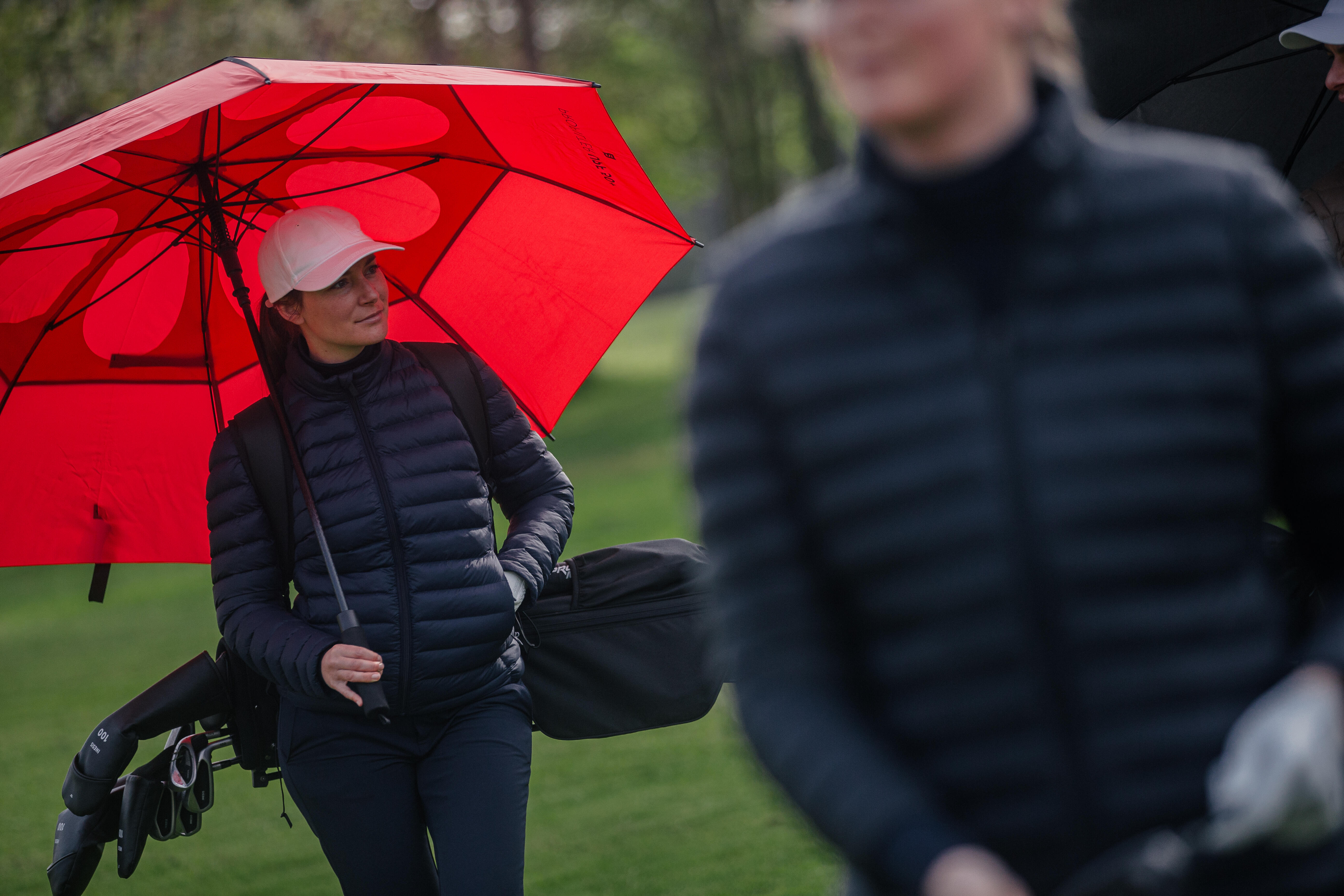 Woman holding a red golf umbrella while carrying golf bag