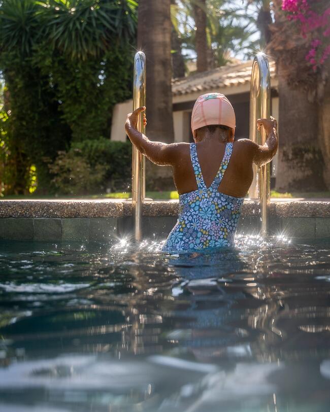 Kind steigt an Leiter aus dem Pool aus, Badeanzug, Badekappe