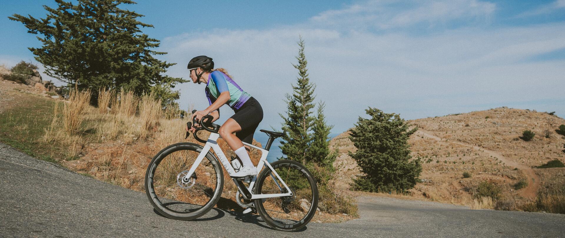 Kobieta w stroju kolarskim jadąca pod górę na rowerze szosowym z oponami bezdętkowymi