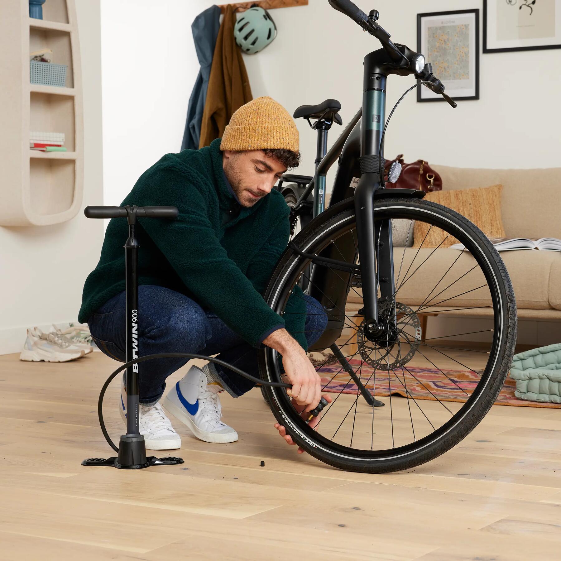 Mężczyzna kucający przy kole rowerowym trzymając pompkę rowerową zastanawiający się jak napompować rower