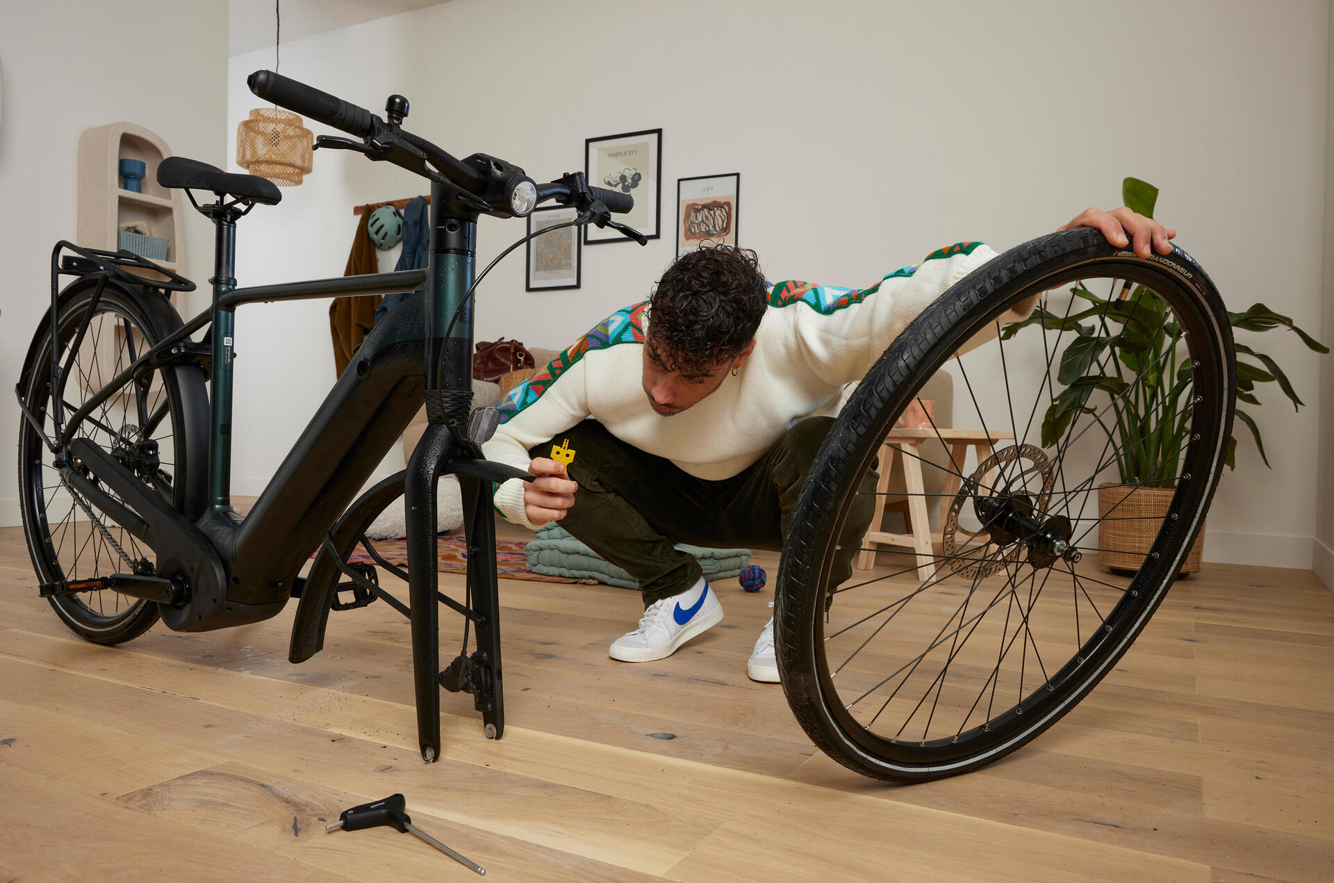 Mężczyzna trzymający ręką odkręconą oponę patrzący na rower