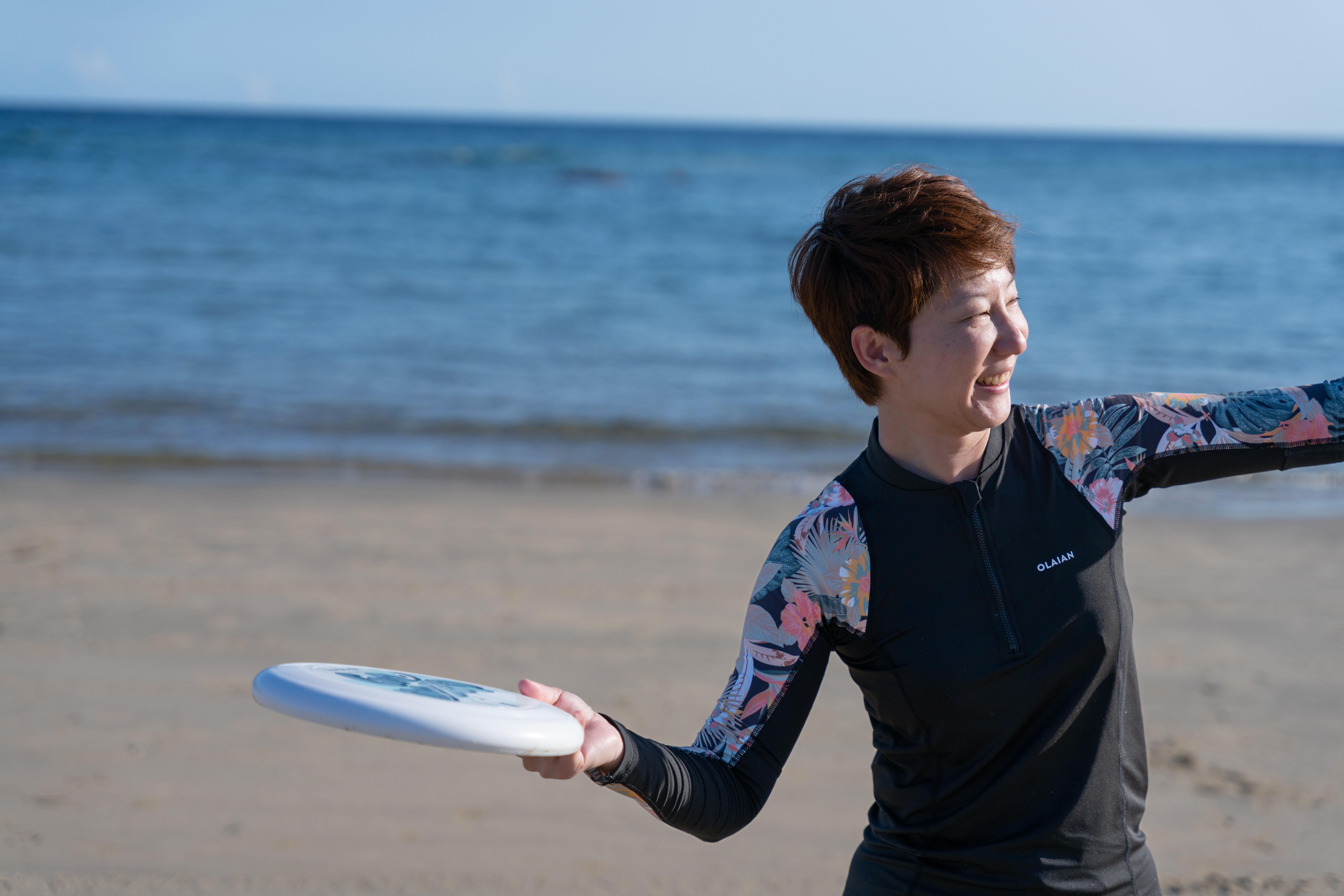 Woman in floral rash guard throwing a white frisbee on the beach
