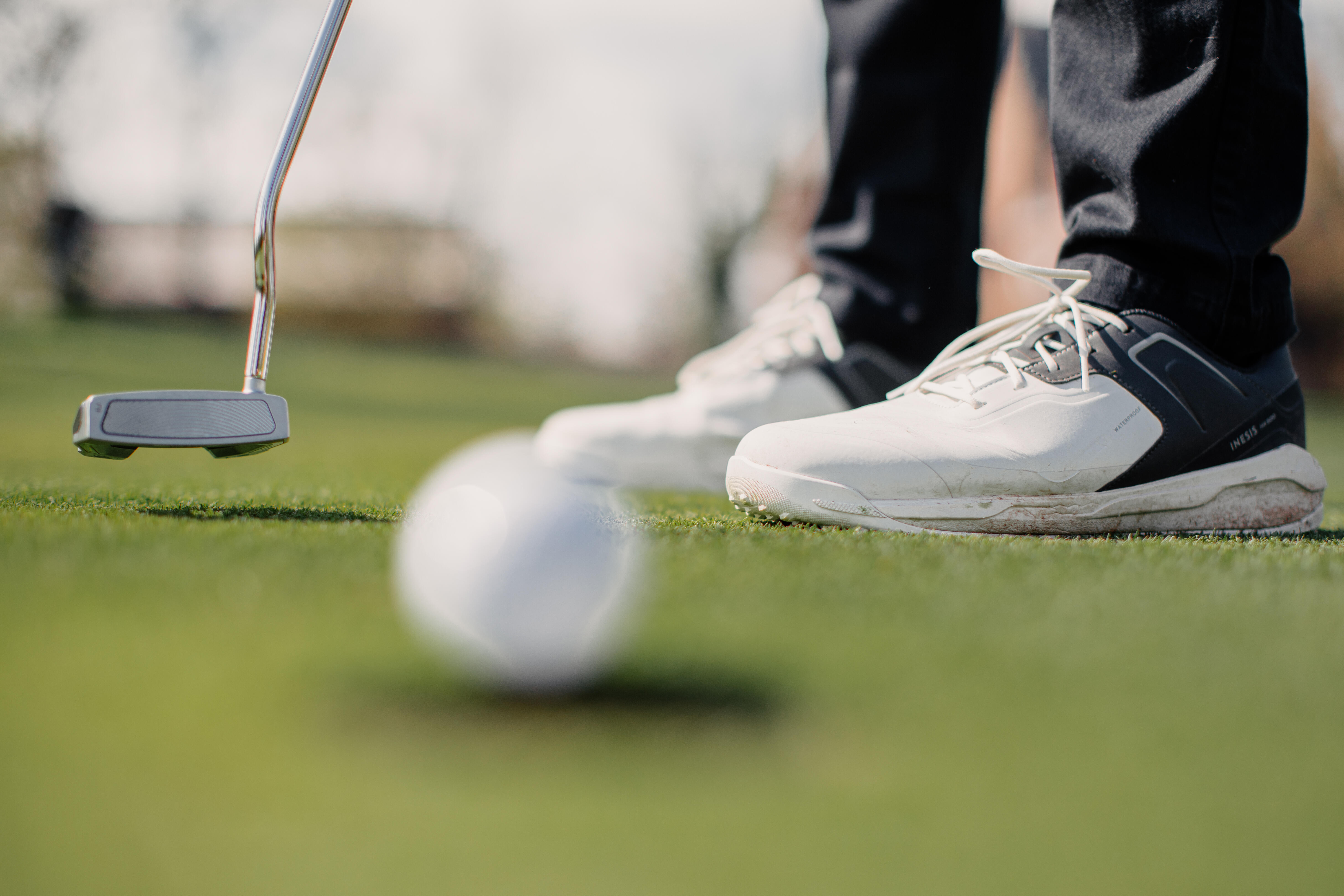 Putter beside golf ball on green, white shoes visible