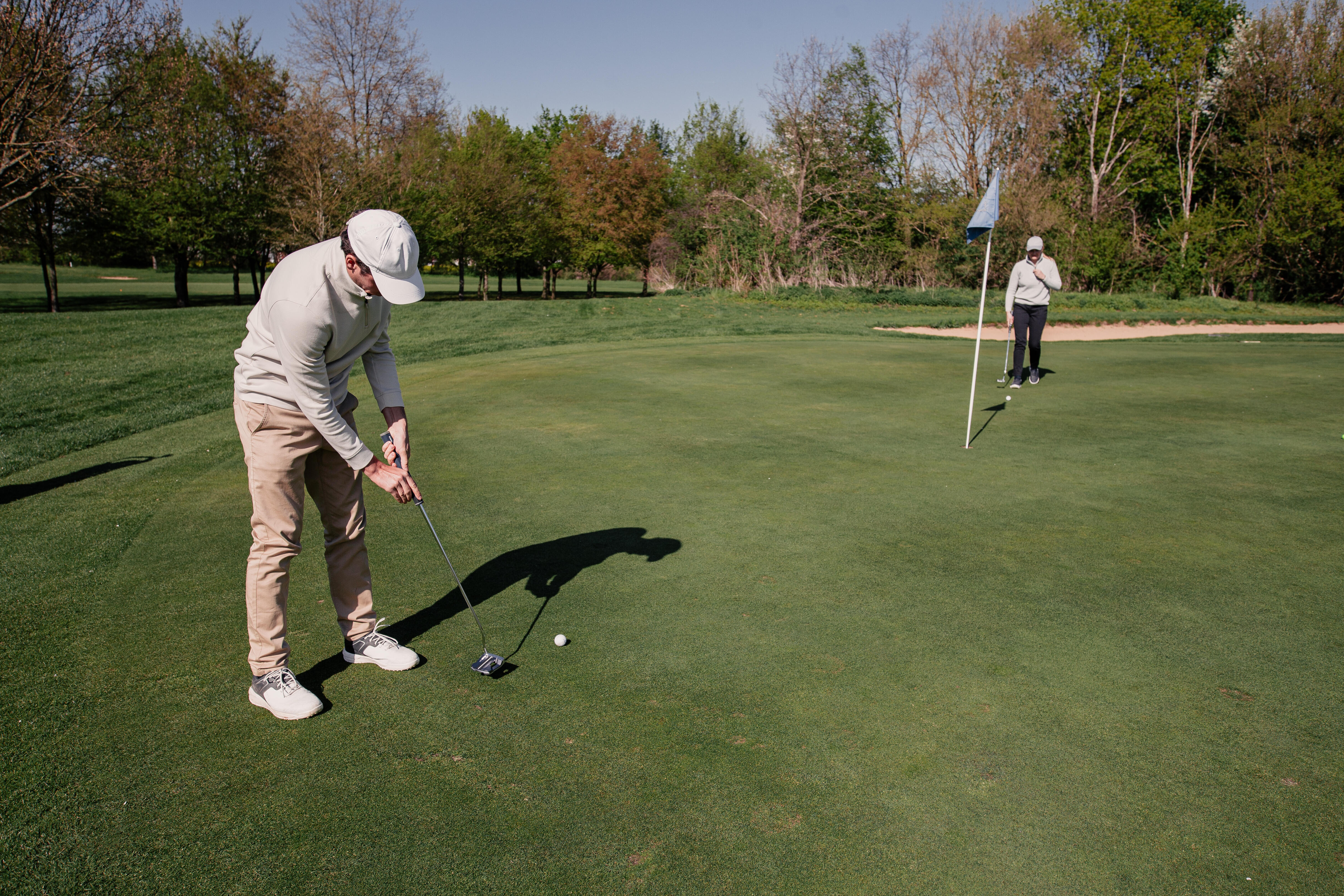 Man putting on the green while another holds the flag
