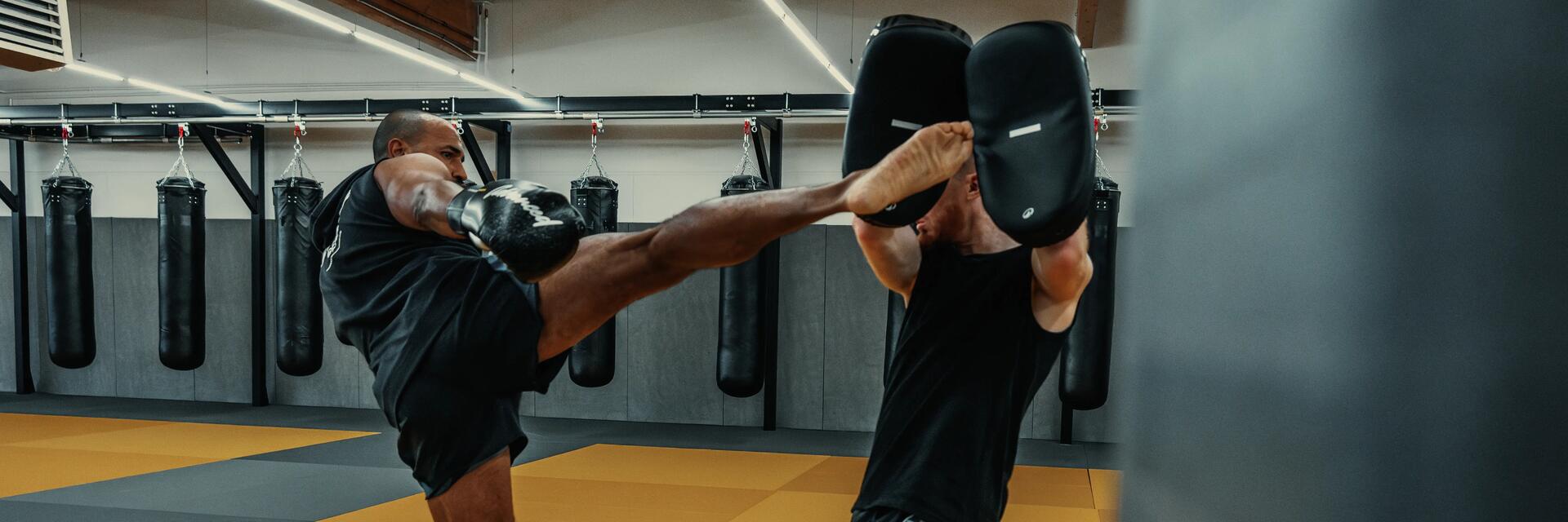 Dwóch mężczyzn trenujących ze sobą kopniecia nogą w kickboxingu na sali