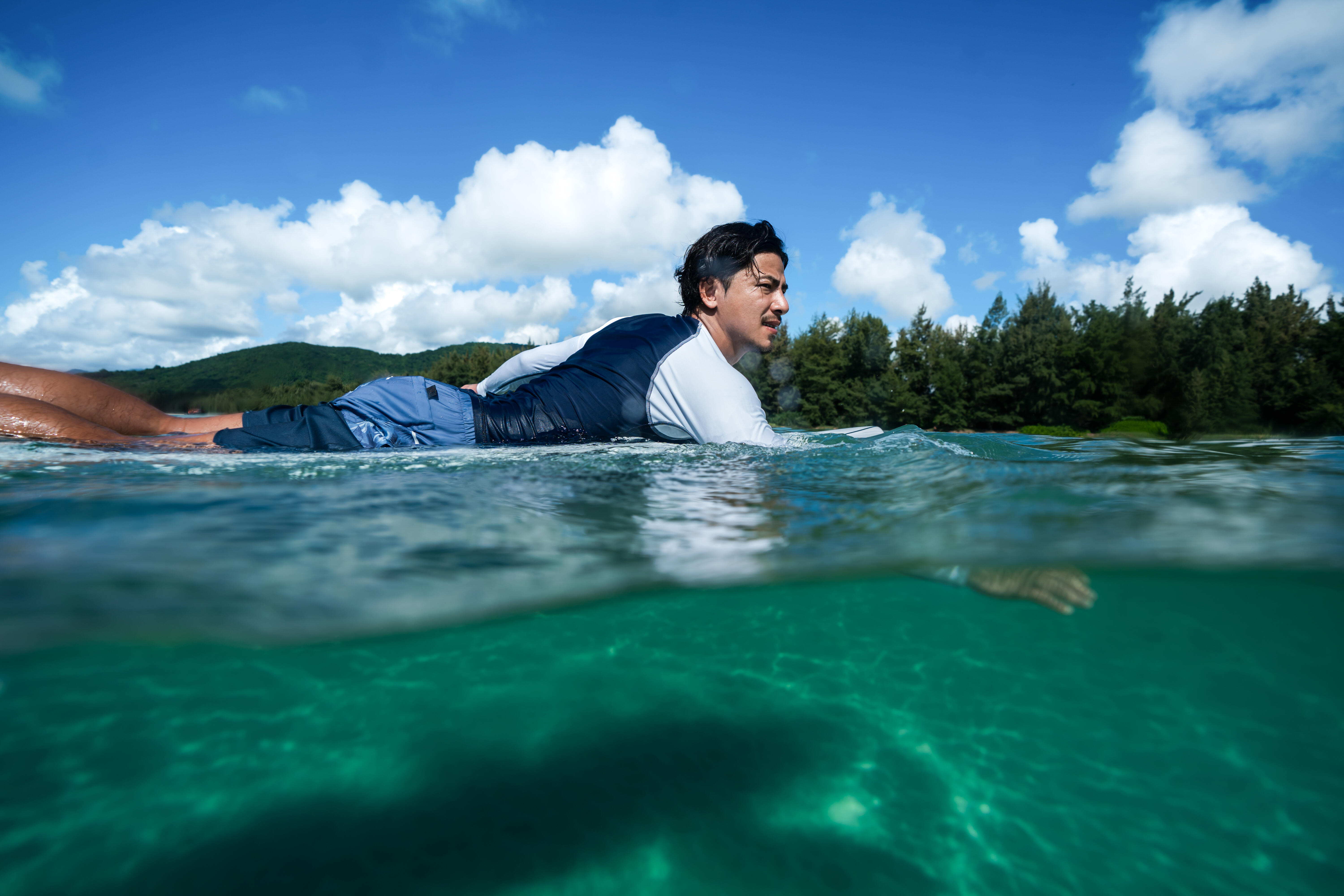 Man paddling on a surfboard wearing a navy and white long-sleeve rash vest.