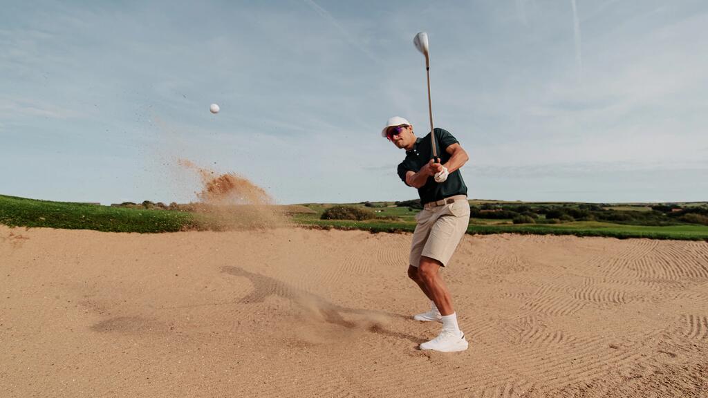 Ein Golfspieler schlägt mit einem Schläger einen Ball und aufwirbelnden Sand aus einem Bunker auf einem Golfplatz.
