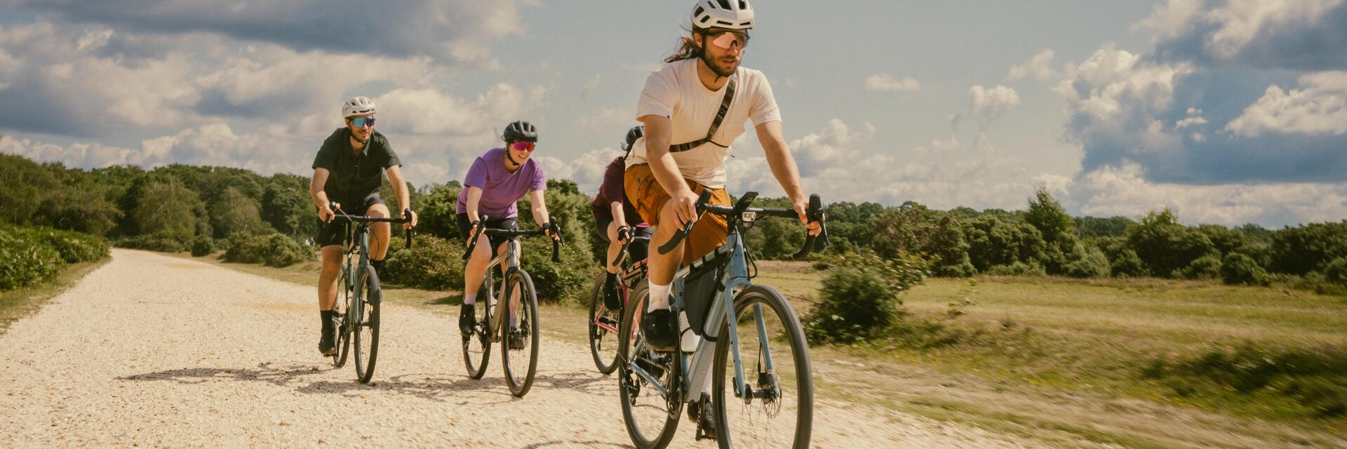 Czworo ludzi w kaskach i w okularach jadącymi rowerami po drodze żwirowej