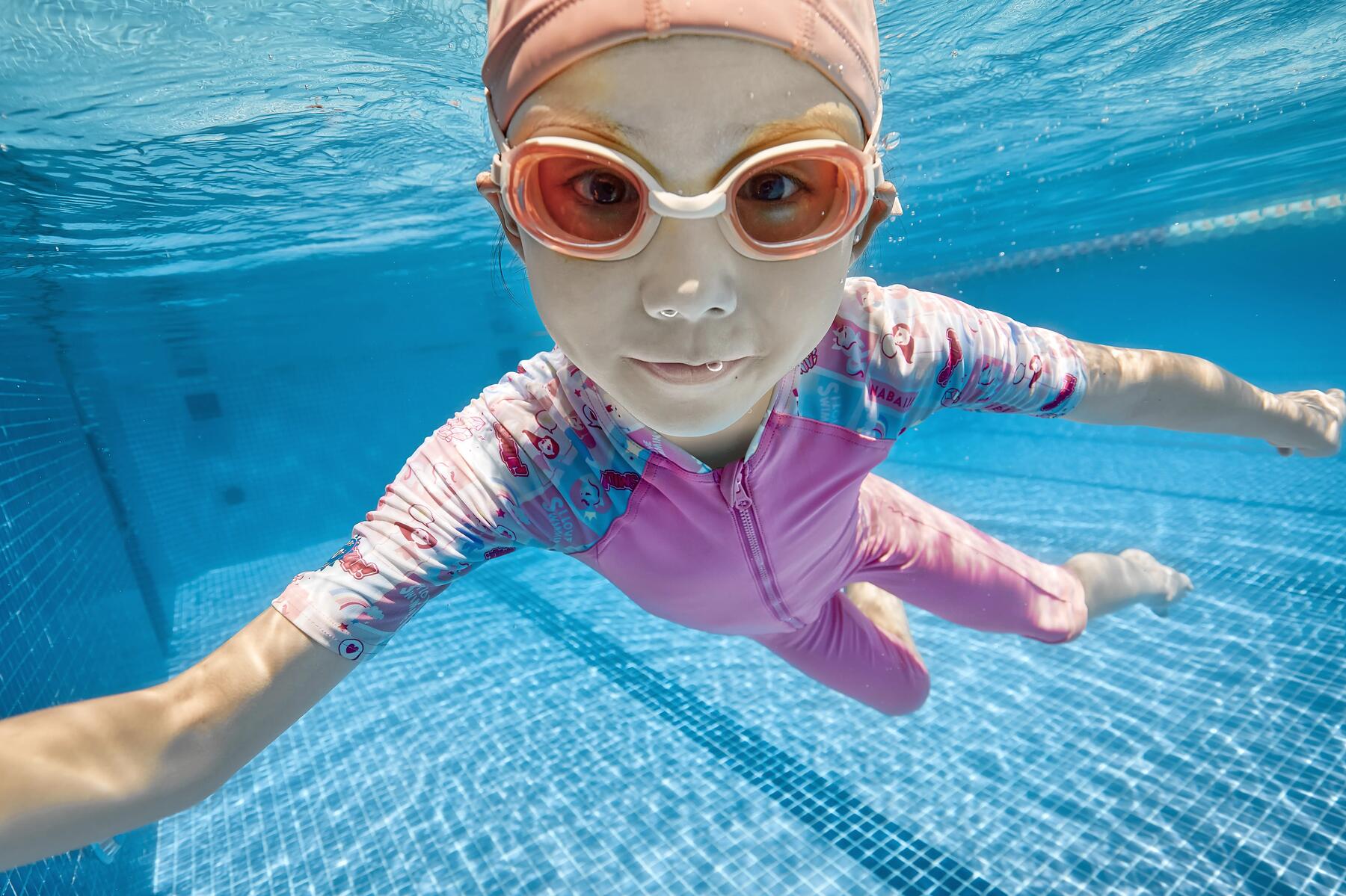 Dziewczynka w czepku i okularkach pływackich pływająca w basenie dbając o aktywność fizyczną