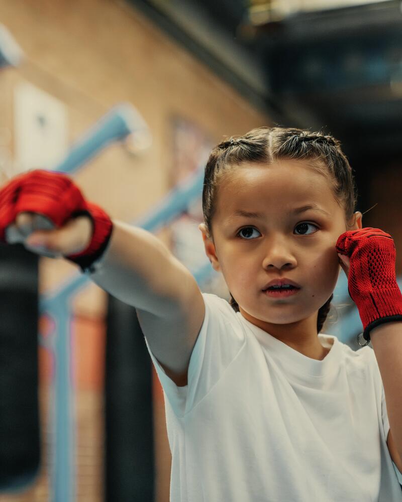 Kind mit geflochtenen Haaren und roten Bandagen an den Händen übt einen Boxschlag in einem Kampfsportstudio.