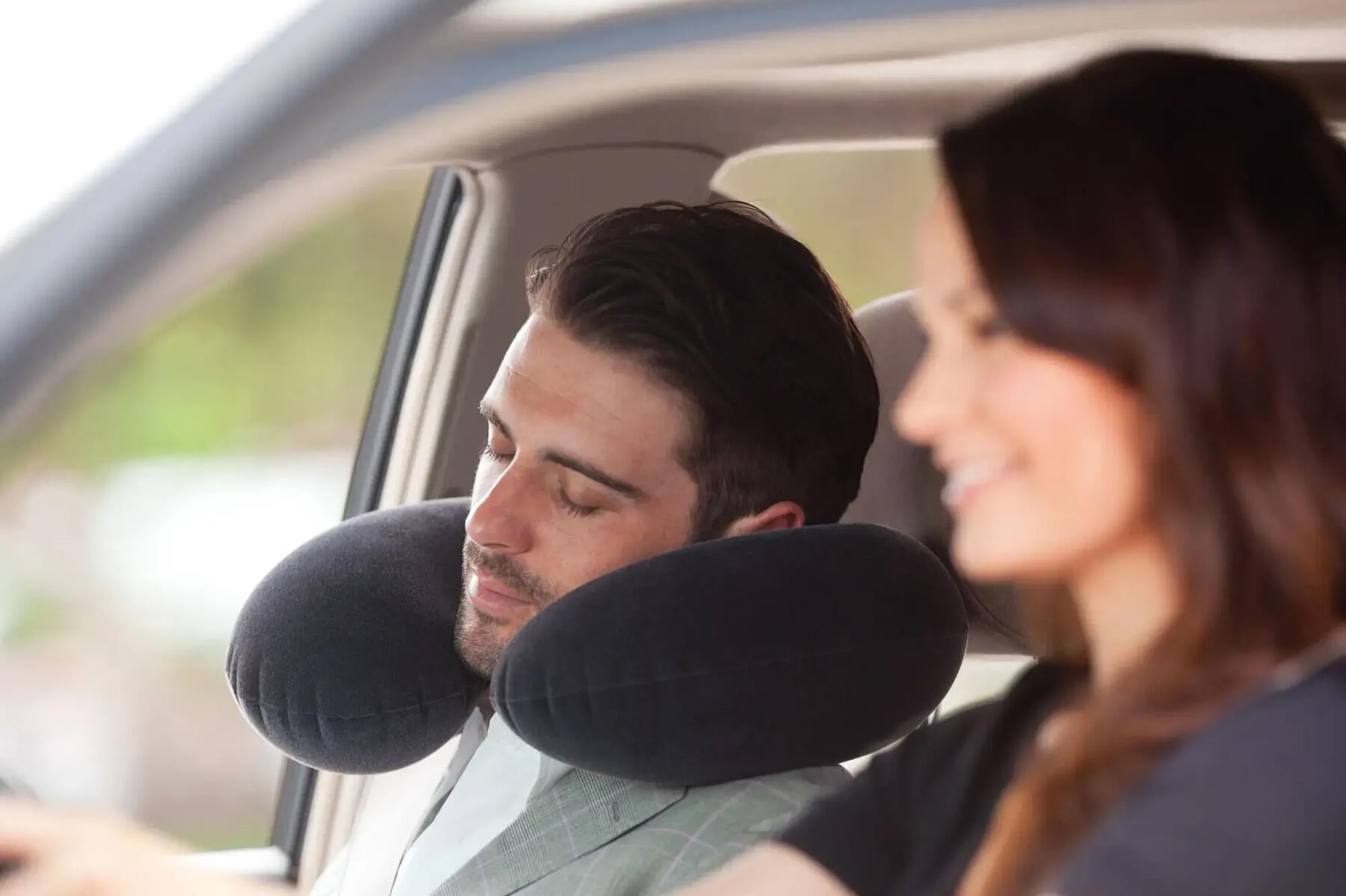 Kobieta prowadząca auto ze śpiącym mężczyzną używającym poduszki podróżnej na miejscu pasażera