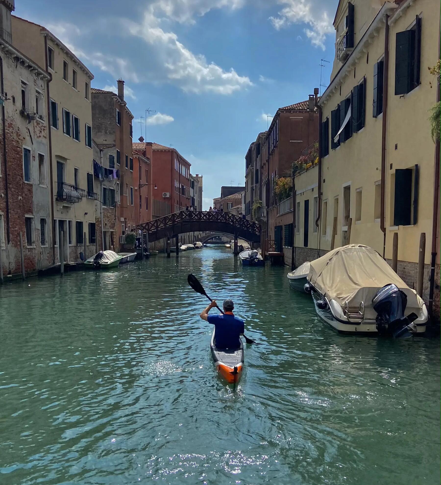 Mann paddelt mit Kanu und Schwimmweste durch Venedig