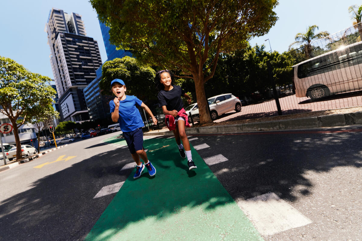Dečak u plavoj majici i prugastim kupaćim gaćama trči i prska vodu u plićaku na sunčan dan.