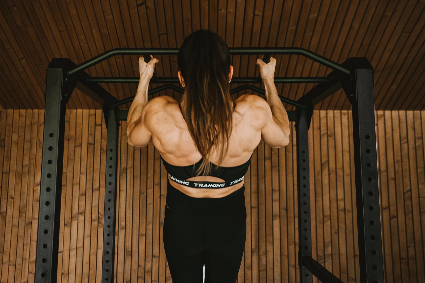 kobieta w legginsach i staniku sportowym przygotowująca się do Runmageddonu wykonując ćwiczenia mięśni rąk na drążku