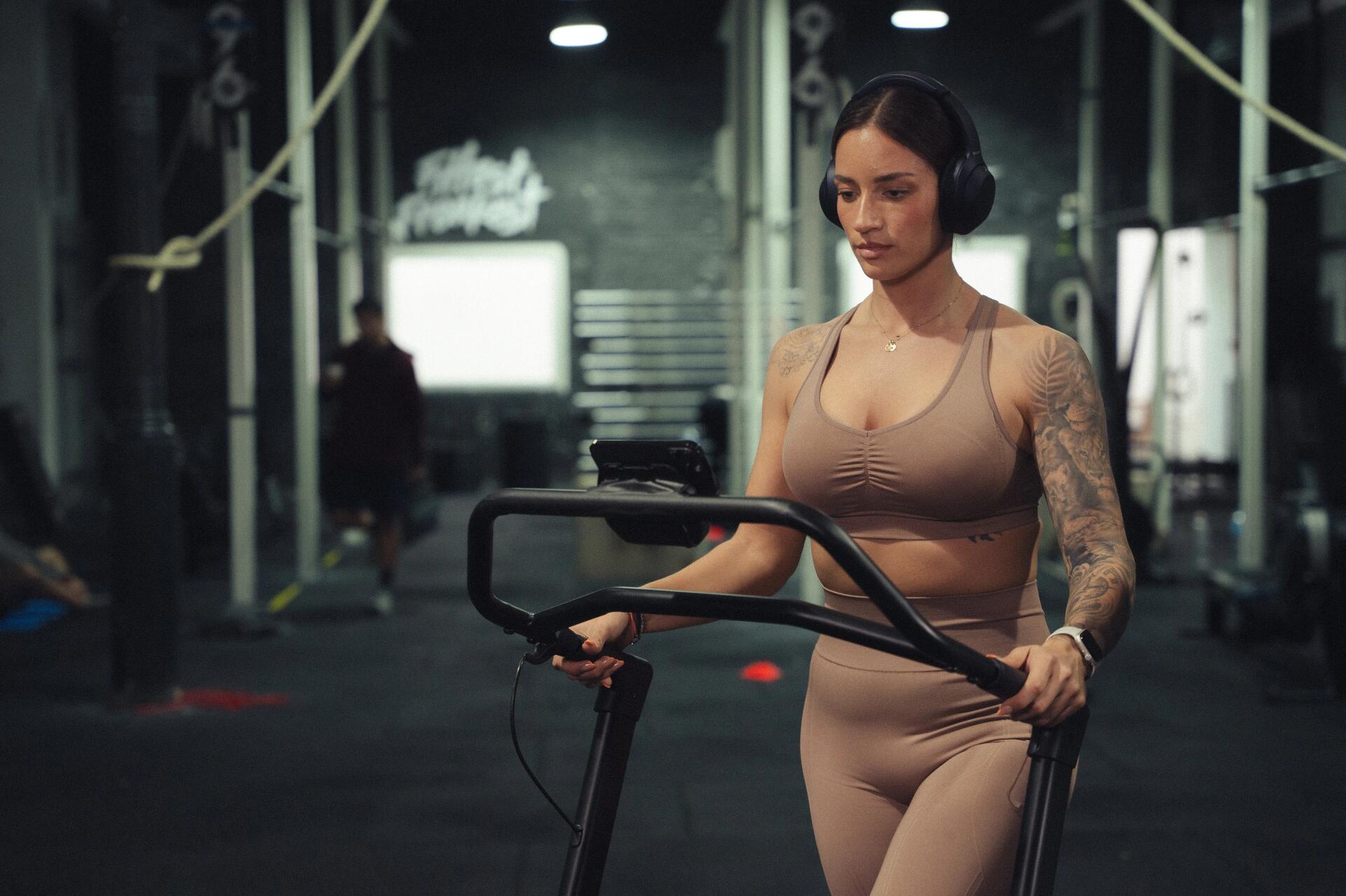 Kobieta w odzieży fitness z słuchawkami na uszach rozpoczynająca trening na bieżni