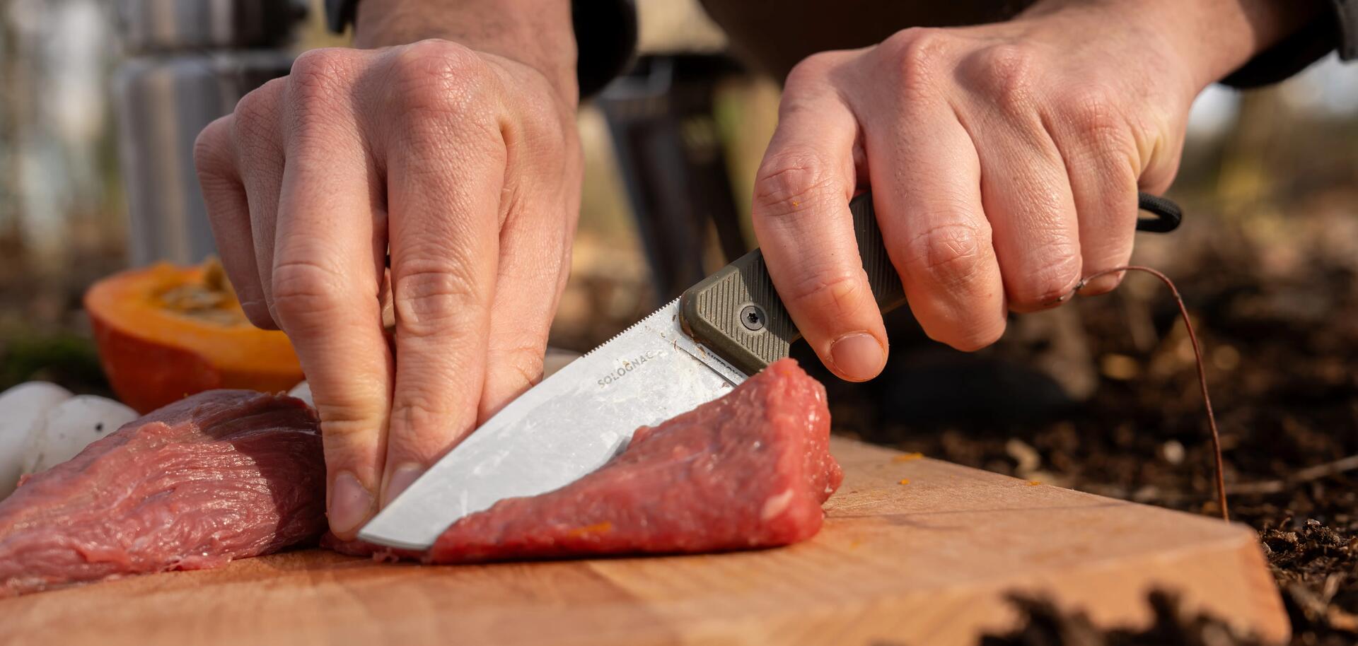 Un chasseur qui coupe de la viande avec un couteau de chasse