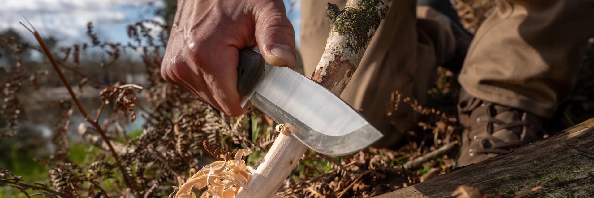 Mężczyzna strugający drewno przy pomocy noża do lasu
