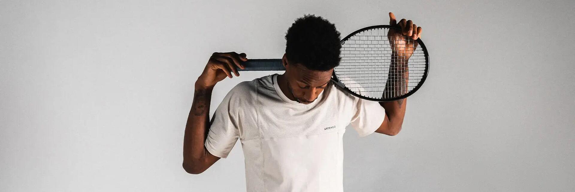 Mężczyzna stojący w koszulce i spodenkach tenisowych opierający o szyję rakietę tenisową z odpowiednim naciągiem  