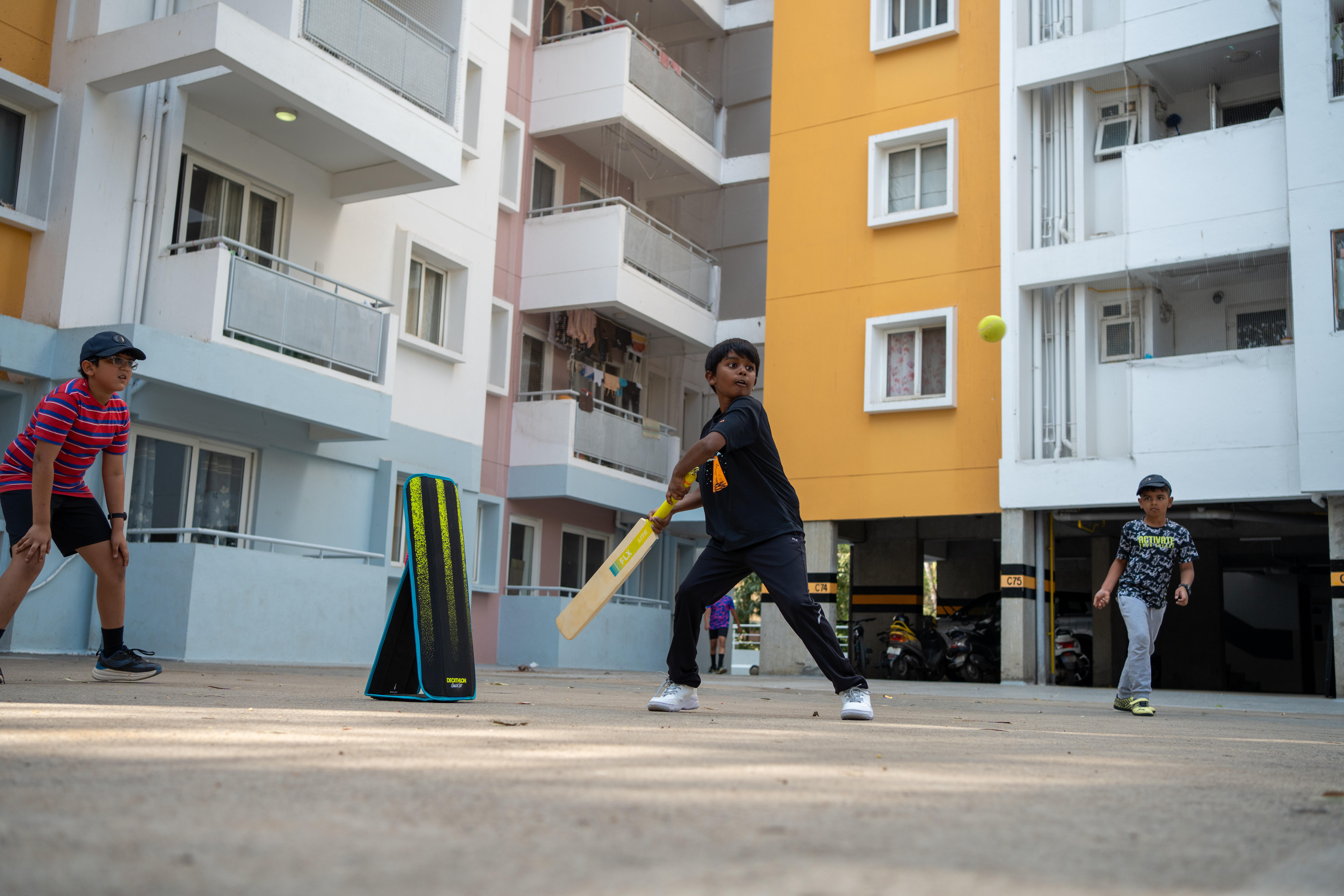 Boy batting with yellow cricket wickets set up in a courtyard
