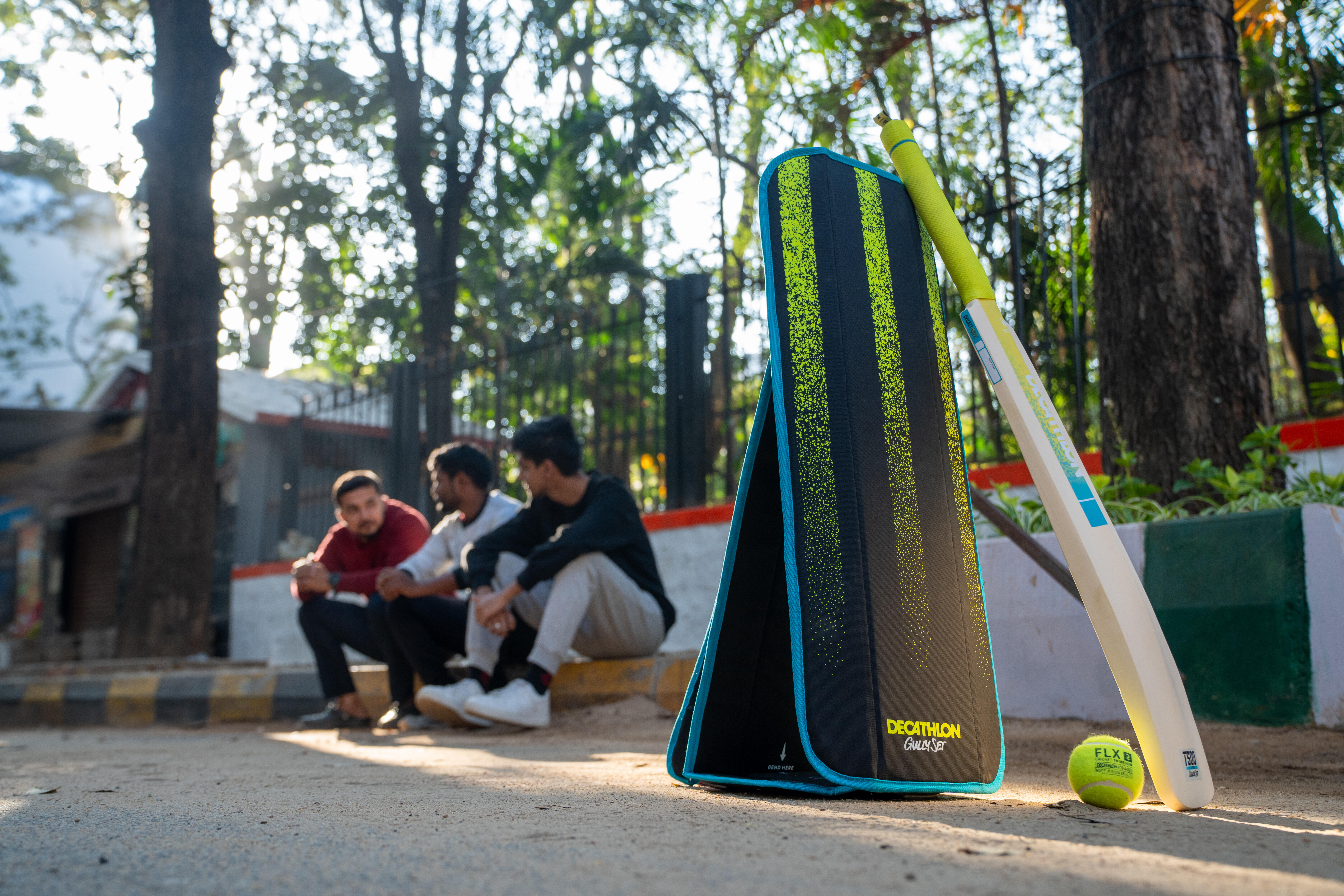 Black and green cricket bag with bat and ball, men sitting nearby