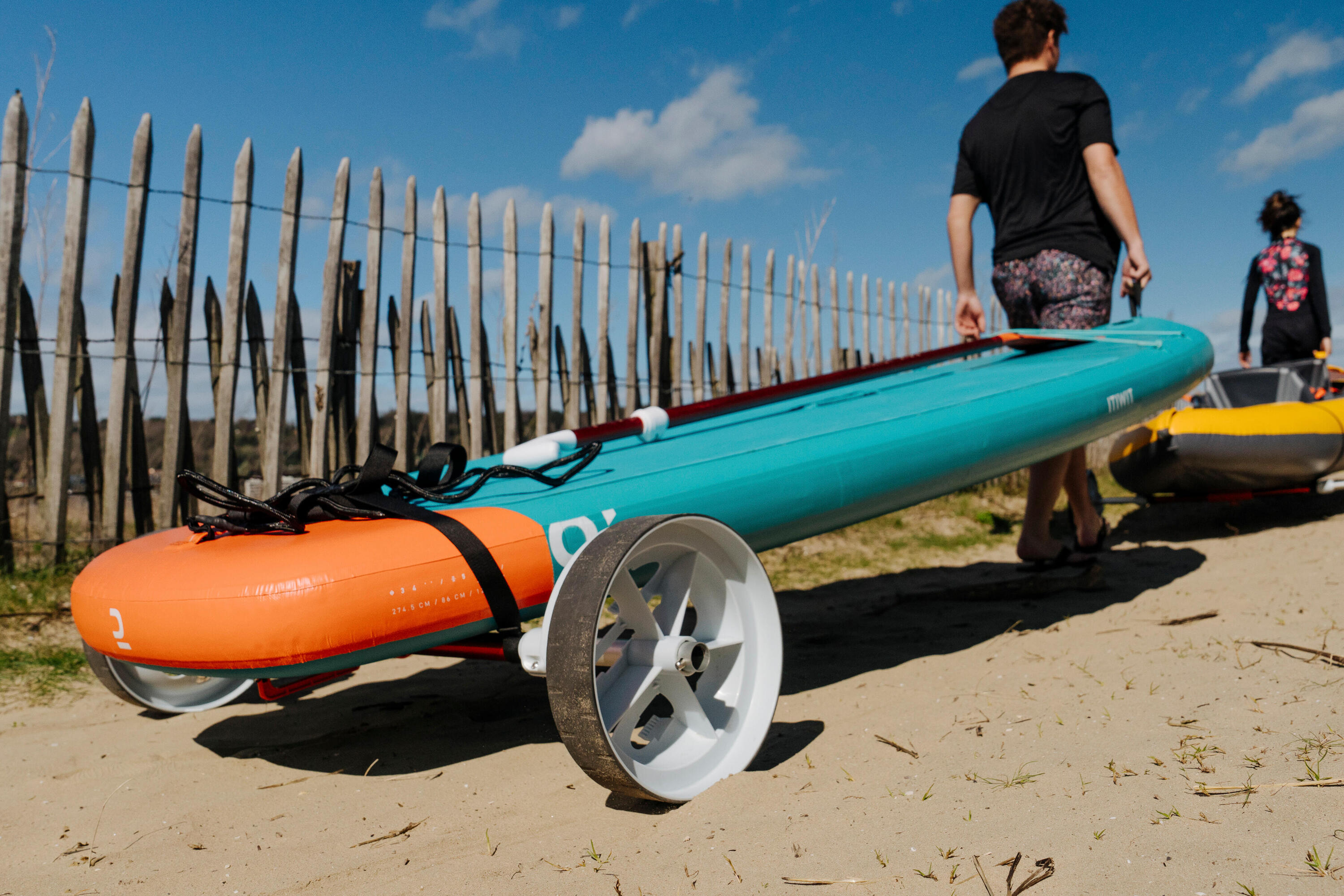 Mann transportiert ein SUP mit einem Trolley über den Strand