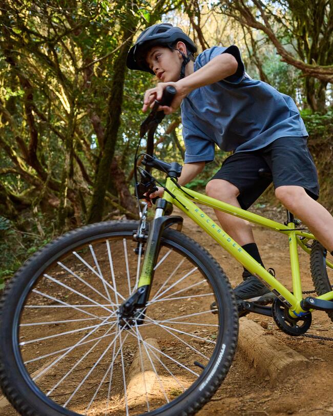 Kind fährt auf gelbem Fahrrad über holperigen Waldweg