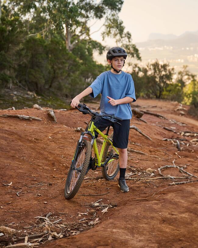 Kind sitzt auf Fahrrad und schaut in die Kamera; im Hintergrund Wald