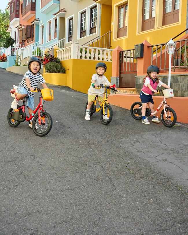 Drei lachende Kinder auf Fahrrädern fahren eine Straße mit bunten Fassaden entlang