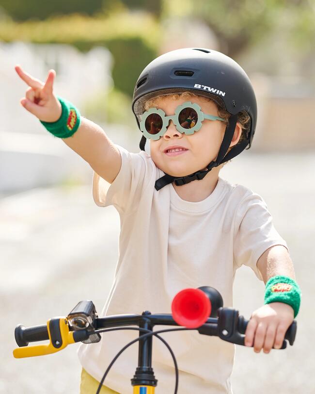 Kind mit Sonnenbrille und Helm sitzt auf Fahrrad und zeigt "Victory-Zeichen"