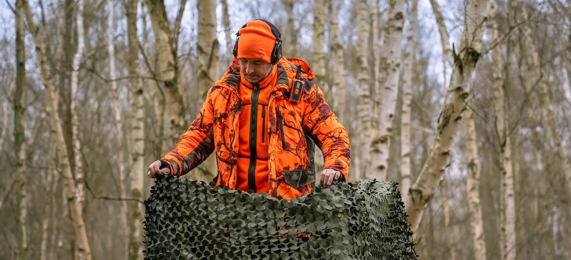 Un chasseur qui s'installe sur son mirador portant une veste et une polaire orange fluo