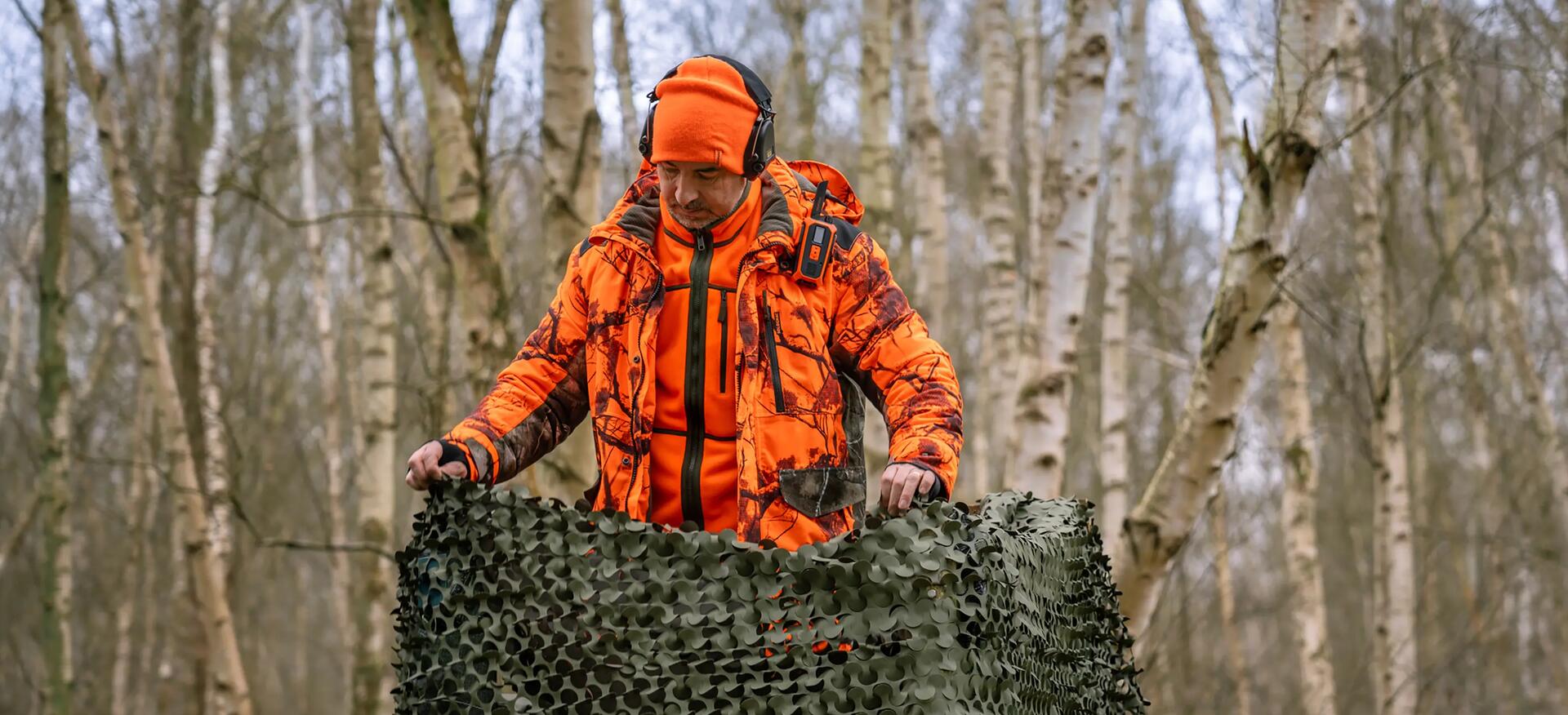 Un chasseur qui s'installe sur son mirador portant une veste et une polaire orange fluo