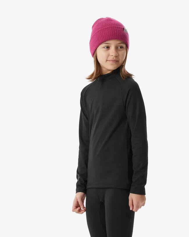Ein Mädchen mit geflochtenen Zöpfen in hellila Baselayer Top und hellblauer Baselayer Hose steht vor einer grauen Leinwand.