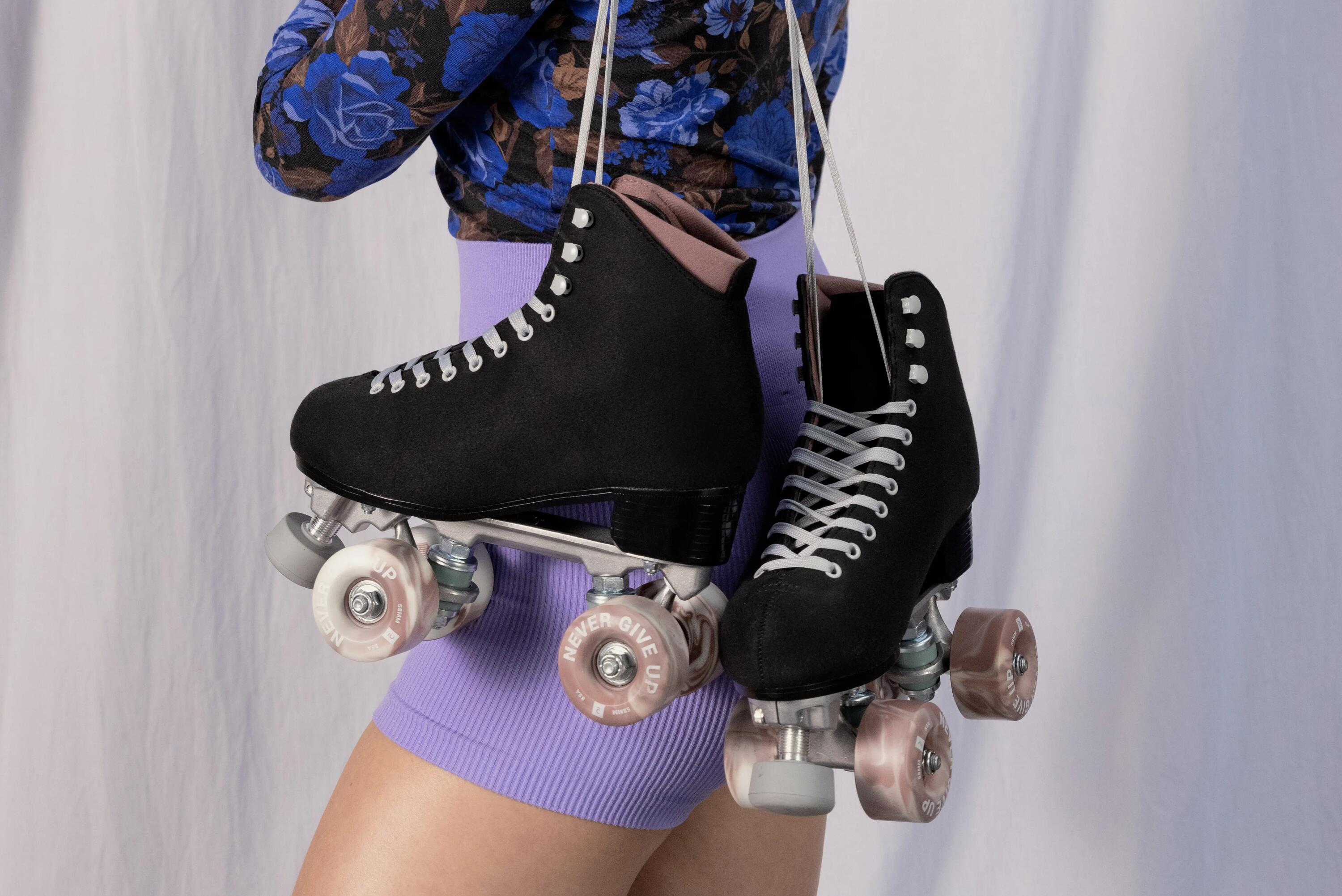 Nahaufnahme einer Person von hinten, die ein Paar schwarze Rollschuhe an den Schnürsenkeln über der Schulter trägt.