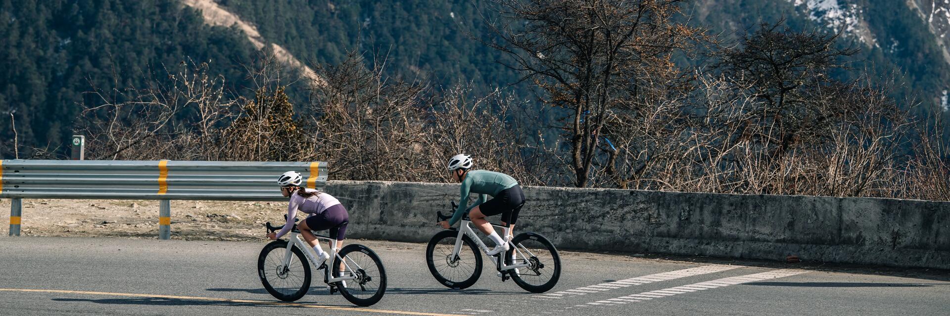 Man and woman road cycling against a a green hilly background