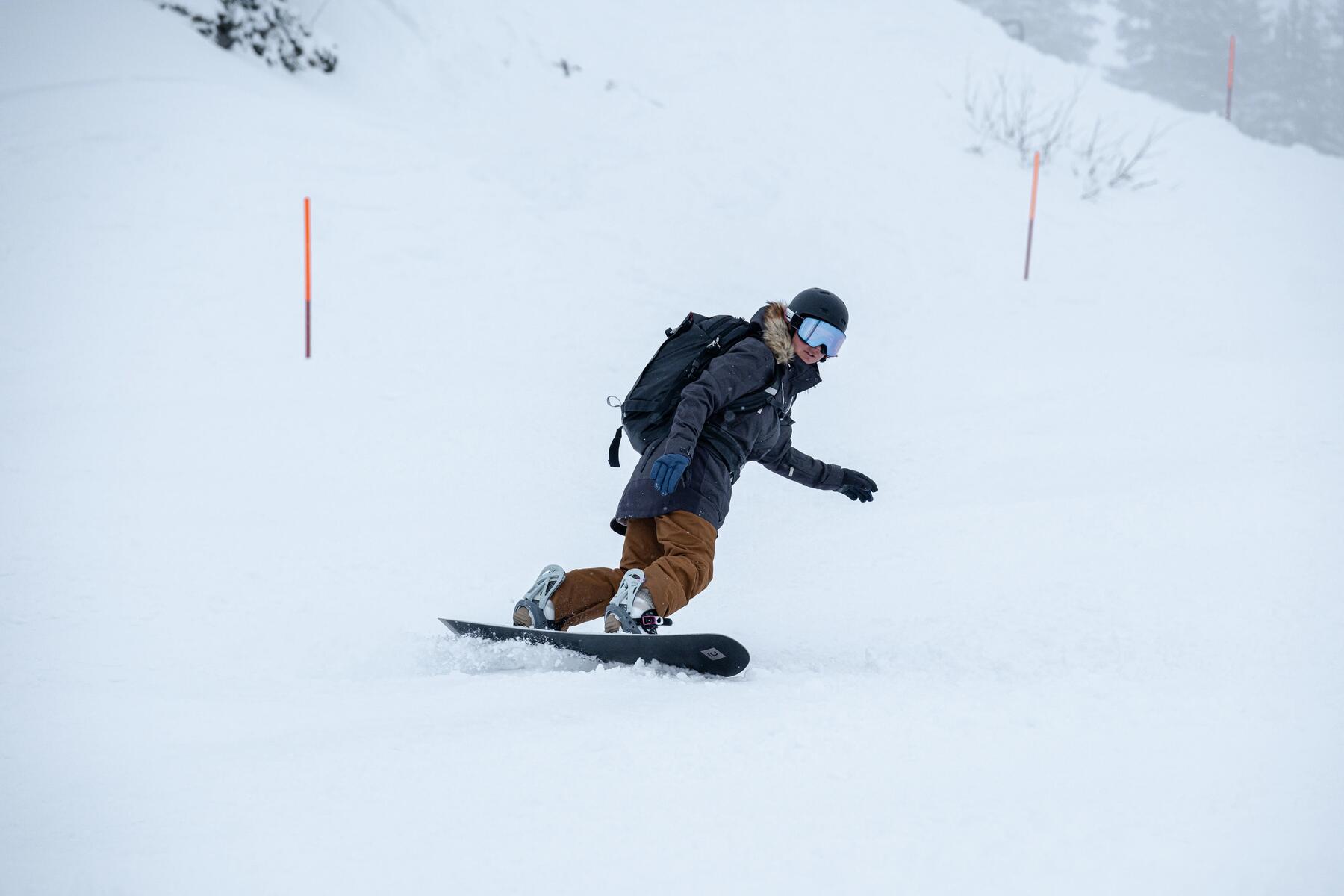 Mężczyzna w kasku i w goglach z plecakiem jeżdżący na snowboardzie