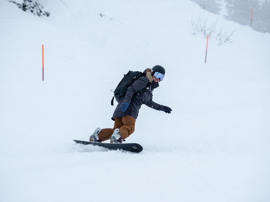 Snowboarder care transportă o placă de snowboard