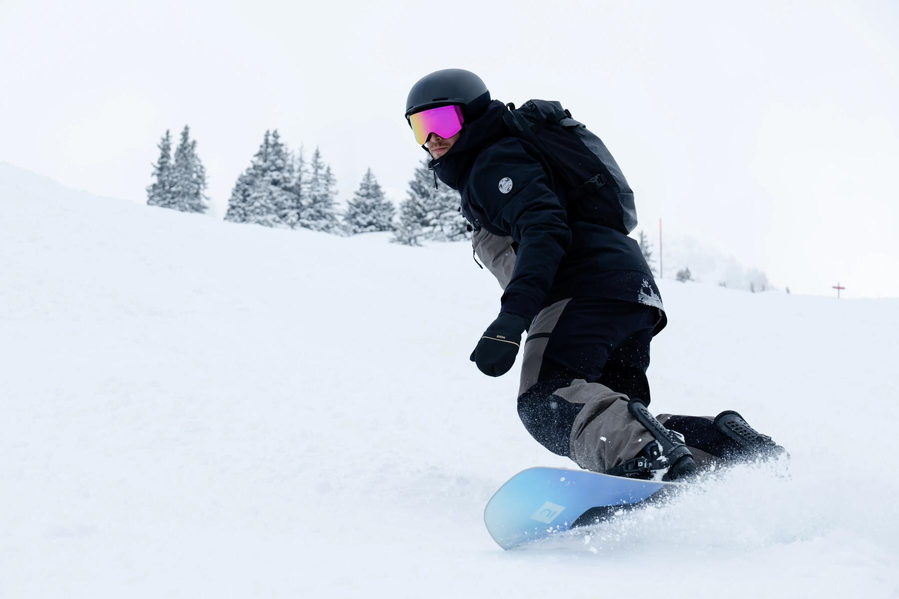 Mężczyzna w odzieży zimowej w kasku i w goglach jadący na desce snowboardowej
